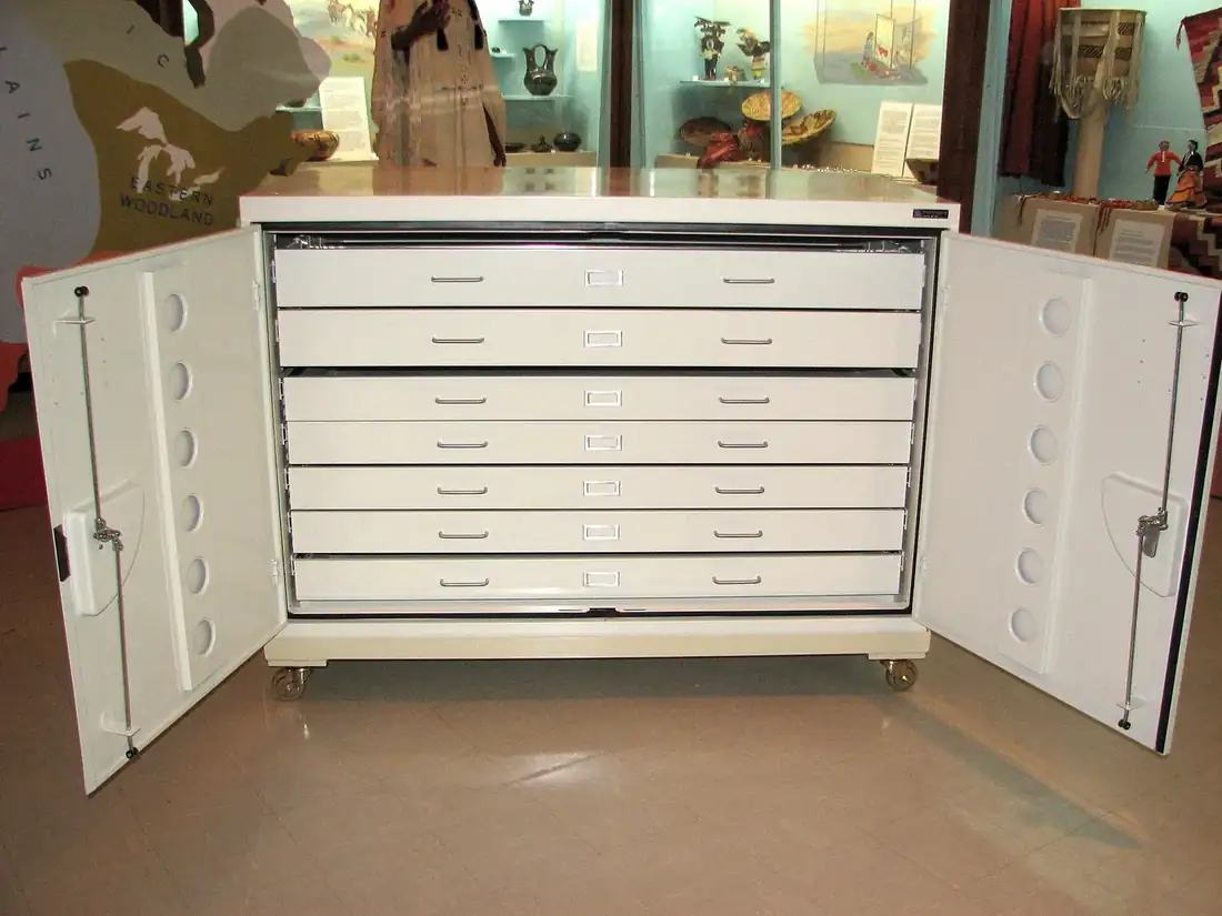 A white cabinet of shallow flat drawers standing open in a museum store